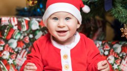 Portrait de heureux petit garçon en costume de Père Noël assis à l'arbre de Noël — Photo de stock