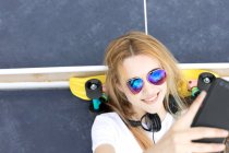 Blonde girl lying on floor on penny board and taking selfie — Stock Photo