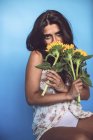 Junge Frau posiert im Studio mit Sonnenblumen auf blauem Hintergrund — Stockfoto
