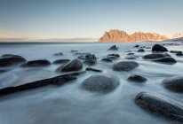 Smooth dark stones in long exposure flow of water on background of cliffs, Lofoten, Norway — Stock Photo