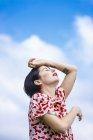 Emotional young woman in patterned dress posing against cloudy sky — Stock Photo