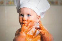 Cheerful toddler boy in apron with dirty face covered with sauce. — Stock Photo