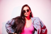 Young pink dressed woman in sunglasses standing at white wall and looking at camera — Stock Photo