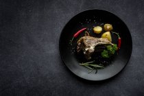 Roast lamb with potatoes on black plate on grey background — Stock Photo