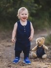 Веселий маленький хлопчик стоїть біля ведмежої іграшки в джинсовому одязі в природі . — стокове фото