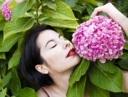 Чуттєва молода жінка торкається рожевої квітки, що росте на кущі — стокове фото