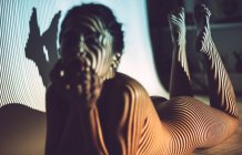 Nackt verführerische junge Frau liegt im Studio mit gestreiften Schatten auf Gesicht und Körper — Stockfoto