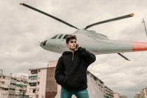 Schöner junger Mann steht am Hubschrauberdenkmal in der Stadt und spricht auf dem Smartphone — Stockfoto