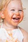 Cheerful toddler boy in apron with dirty face covered with sauce. — Stock Photo