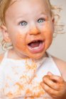 Niño alegre en delantal con la cara sucia cubierta de salsa. - foto de stock