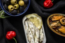 Peperoni e olive vicino a pesce in scatola su tessuto nero — Foto stock