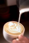 Cortar la mano de camarero irreconocible verter crema al café con leche y dibujar una flor. - foto de stock