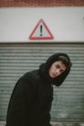Adolescente pensieroso in giacca nera con cappuccio in piedi sulla strada con segno esclamativo e guardando la fotocamera — Foto stock