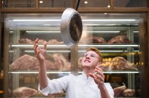 Cocinero en vasos y vestido blanco vomitando sartén trabajando en restaurante. - foto de stock