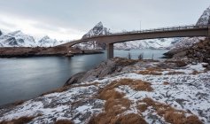 Vista pitoresca de montanhas nevadas e mar com ponte sobre fundo — Fotografia de Stock