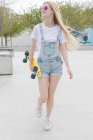 Blonde stylish girl with penny board walking in park — Stock Photo