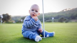 Jovem sentado no gramado verde no buraco no clube de golfe e olhando para a câmera. — Fotografia de Stock