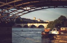 Старый каменный мост над рекой и лодки, плавающие возле набережной, Париж, Франция — стоковое фото