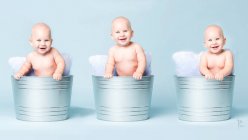 Fröhliche nackte Kleinkinder sitzen in metallischen Eimern mit Kissen. — Stockfoto