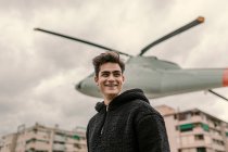 Смеющийся молодой человек, стоящий у памятника вертолету на городской улице — стоковое фото