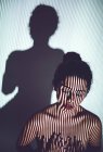Гола молода жінка покриває груди руками в студії червоними губами і смугастою тіні на обличчі і тілі — стокове фото