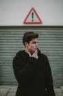 Adolescent réfléchi en veste à capuche noire debout sur la rue avec signe d'exclamation et regardant loin — Photo de stock