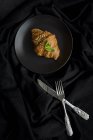 Croissant al forno su piastra su tessuto nero con coltello e forchetta — Foto stock