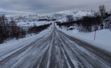 Vue en perspective de la route froide dans un terrain enneigé au crépuscule sombre, Lofoten, Norvège — Photo de stock