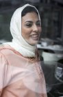 Femme marocaine souriante avec hijab assis derrière la vitre — Photo de stock