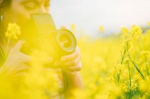 Woman retro camera making photo in nature with yellow flowers close up — Stock Photo