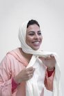 Lächelnde marokkanische Frau in typisch arabischem Kleid, die Hijab auf weißem Hintergrund bindet — Stockfoto