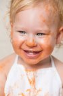 Веселий маленький хлопчик в фартусі з брудним обличчям, вкритим соусом . — стокове фото