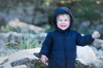 Alegre niño pequeño mirando a la cámara y sosteniendo bola de nieve en la naturaleza. - foto de stock