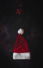 Red and white santa claus hat and star shaped christmas ornament on dark background — Stock Photo