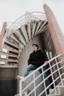Молодой улыбающийся мужчина стоит на лестнице здания и смотрит в сторону — стоковое фото