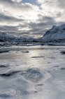 Couche de glace fissurée sur l'eau avec des montagnes enneigées — Photo de stock