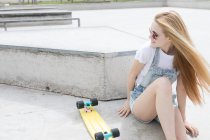 Девочка-блондинка, сидящая на полу с пенни-доской — стоковое фото