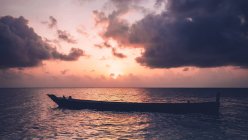 Bateau vide flottant dans l'océan sous le ciel nuageux et le coucher du soleil. — Photo de stock