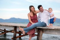 Happy mother and father sitting with little boy on wooden pier. — Stock Photo
