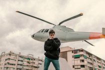 Красивый молодой человек стоит у памятника вертолёту на городской улице — стоковое фото