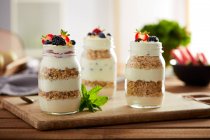 Glass jars with granola and yogurt on wooden board — Stock Photo