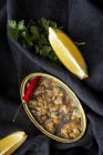 Blechdose mit köstlichen Meeresfrüchten serviert mit Paprika und Zitrone auf schwarzem Stoff — Stockfoto