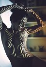 Обнаженная юная соблазнительная женщина с красными губами и полосатой тенью на лице и теле, позирующая в студии — стоковое фото