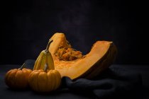 Fresh whole pumpkins with piece on cloth on black background — Stock Photo