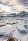 Vista di ghiaccio incrinato con copertura di neve sulla superficie dell'acqua contro le montagne, isola di Lofoten — Foto stock