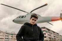 Красивый молодой человек стоит у памятника вертолёту на городской улице — стоковое фото