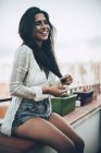 Young laughing woman in shirt and denim shorts sitting at balcony — Stock Photo