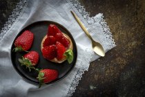 Delicioso postre lleno de crema y fresas frescas en plato negro en servilleta blanca - foto de stock