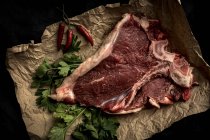 Steak de bœuf cru sur parchemin avec des ingrédients sur fond noir — Photo de stock
