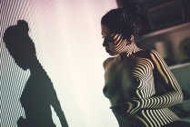 Обнажённая юная соблазнительная женщина позирует в студии с полосатой тенью на лице и теле — стоковое фото